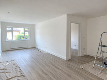 Freshly plastered white room with grey flooring, a doorway, and a stepladder after renovation.